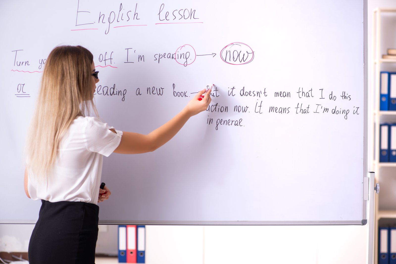 professora escrevendo a explicação de gramática no quadro durante uma aula